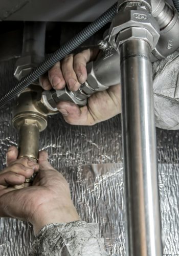 Close-up of a plumber's hands installing steel pipes indoors, showcasing skilled manual work.
